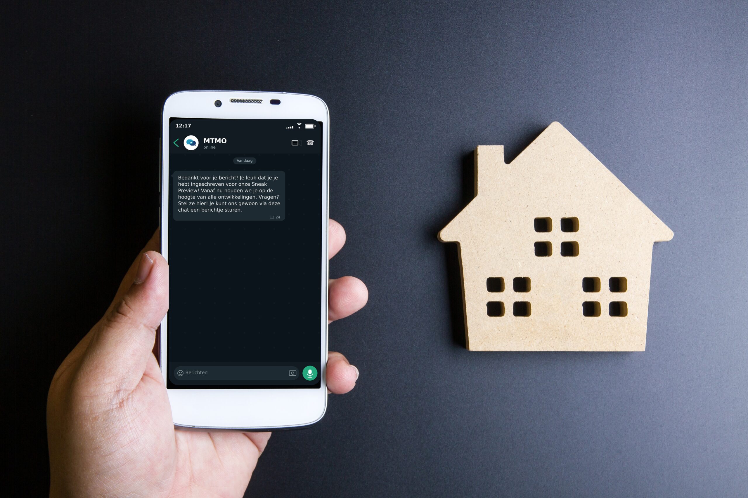 Kartonnen huis en een telefoon in de hand met een Sneak Preview WhatsApp-bericht