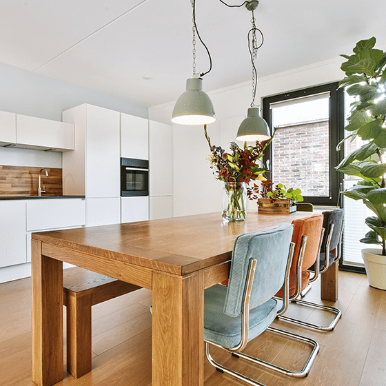 Eethoek met houten eettafel en een moderne witte keuken met inbouwapparatuur